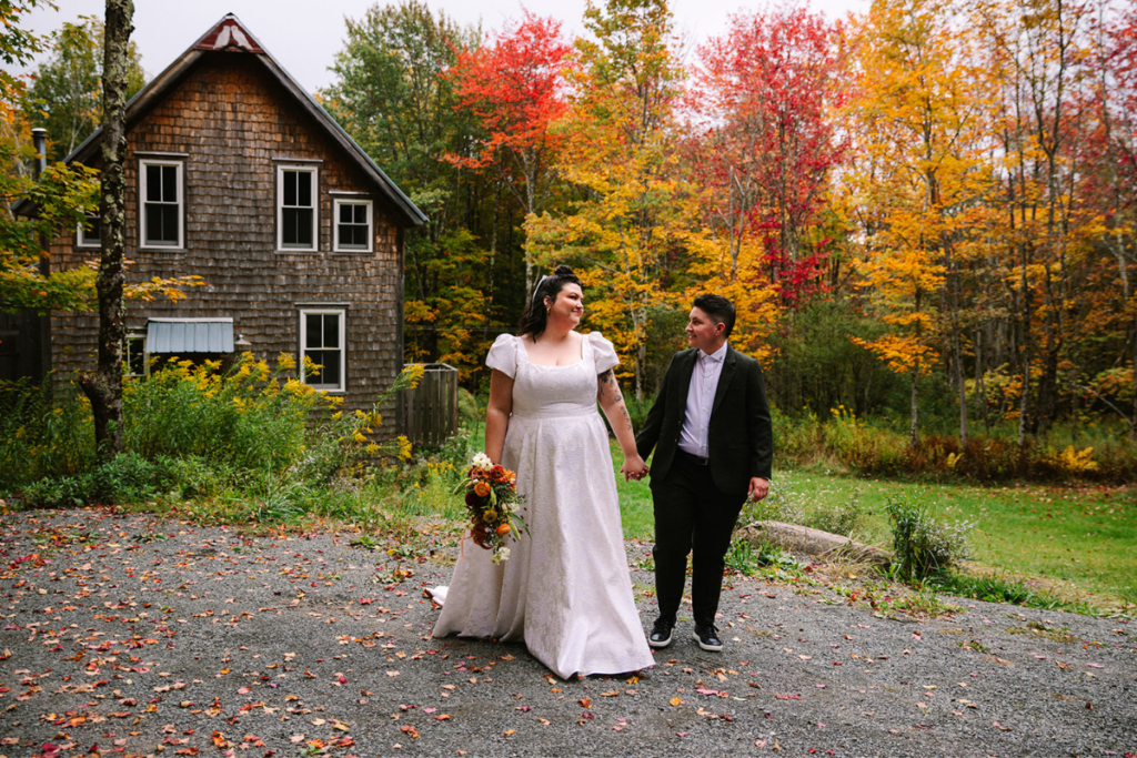 wedding couple holding hands in front of a barn and fall foliage